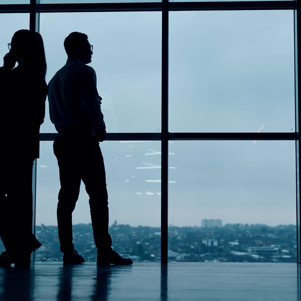 Siluetas de personas de negocios trabajando en la oficina con ventana panorámica. Un hombre bebe café y una mujer tiene una conversación telefónica.