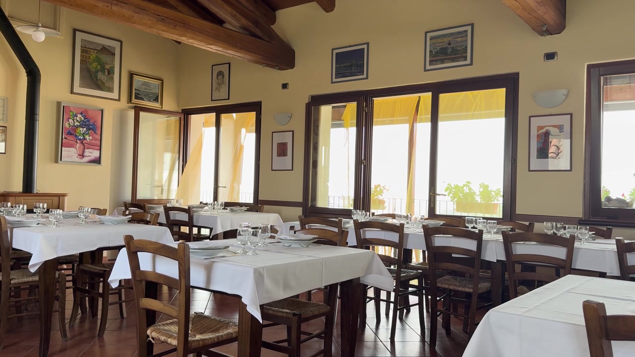 Inquadratura ampia statica di una sala da pranzo tradizionale europea con tavoli apparecchiati e luce naturale.