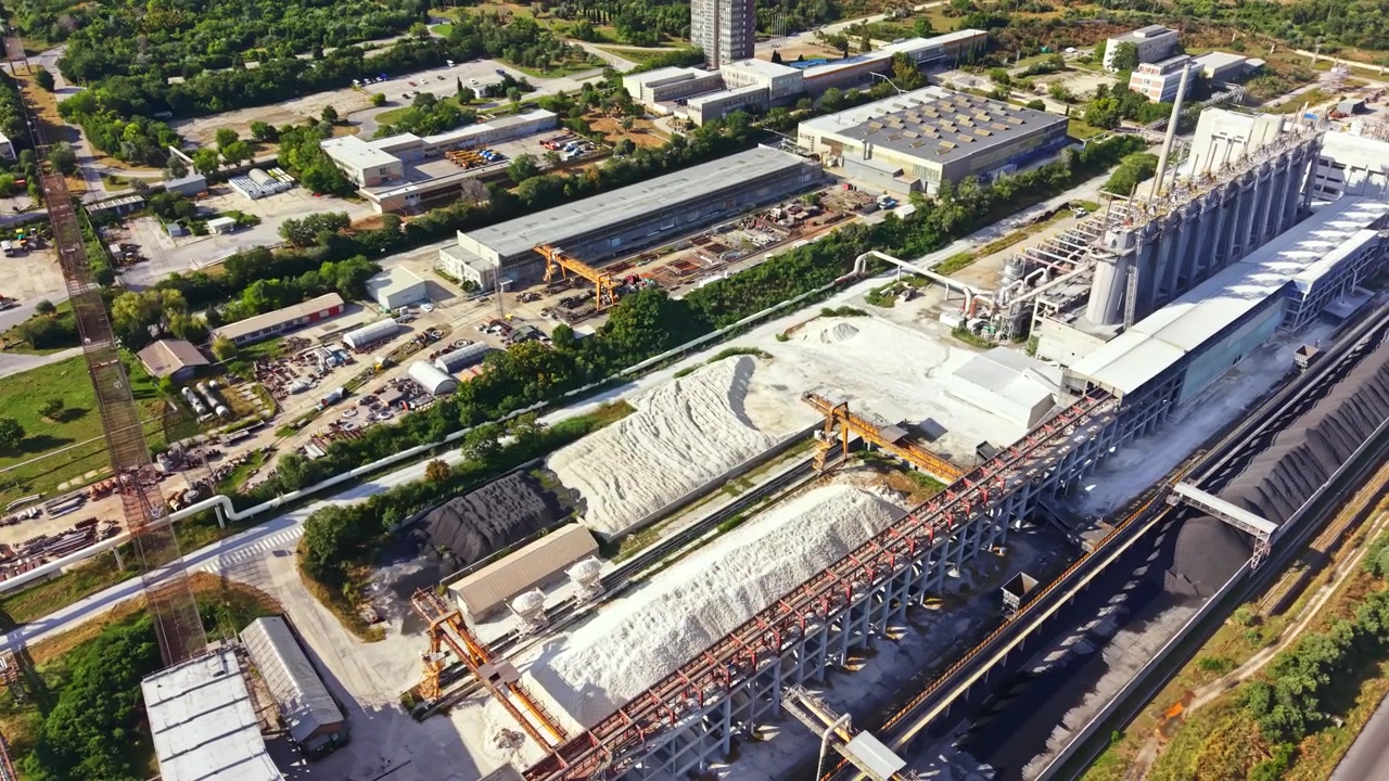 Vista di un grande sito industriale con vari edifici, macchinari e materiali di giorno