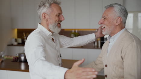 two happy senior men friends greeting each other with a hug and talking at home 1