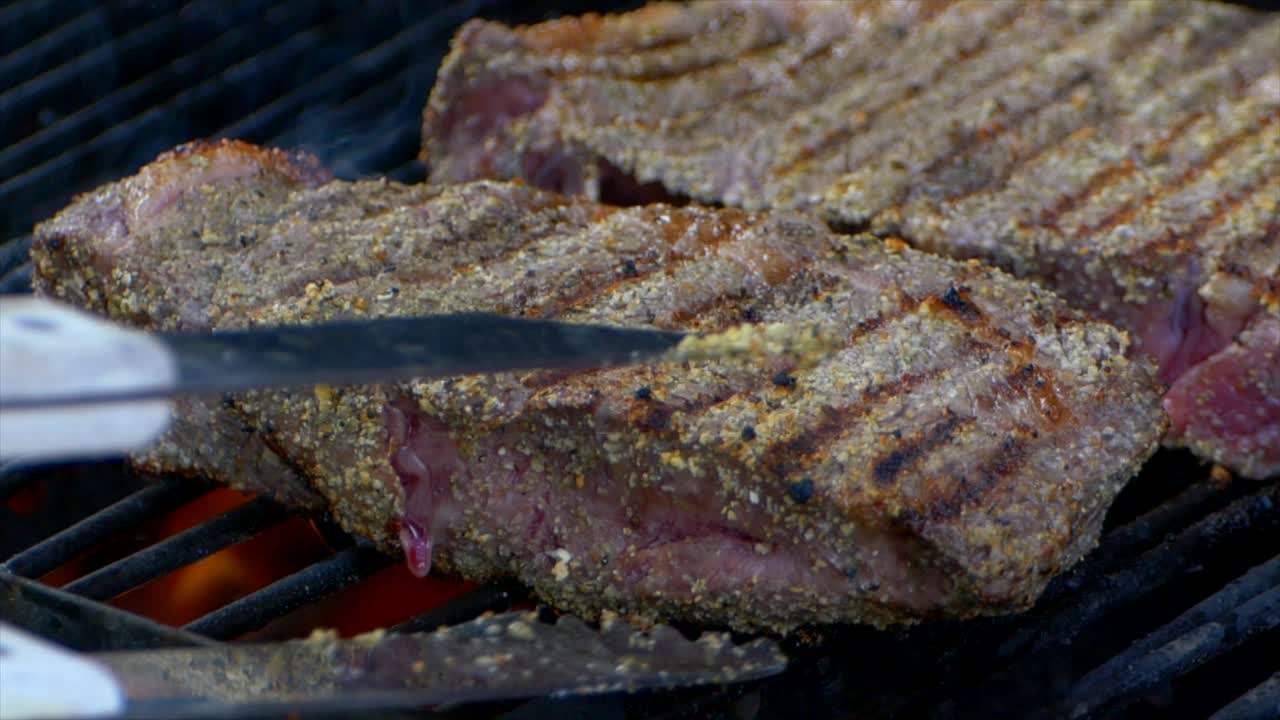 un par de pinzas para carne empujan un jugoso filete de costilla casi cocido en una parrilla y lo deslizan un poco