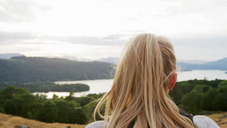 A-young-blonde-woman-standing-at-the-summit-the-view-during-a-mountain-hike,-close-up,-back-view