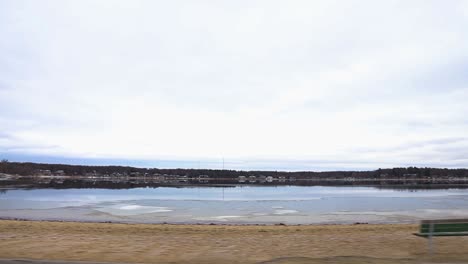 driving on a road parallel to a small lake with many vacation homes on the lakeshore facing the lake