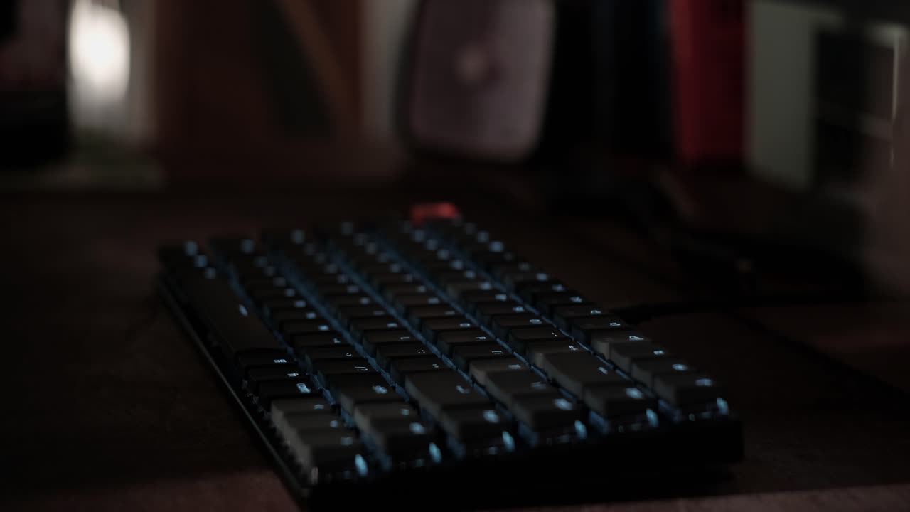 Close-up static shot of hands typing on a mechanical keyboard and leaving the desk in a dimly lit workspace