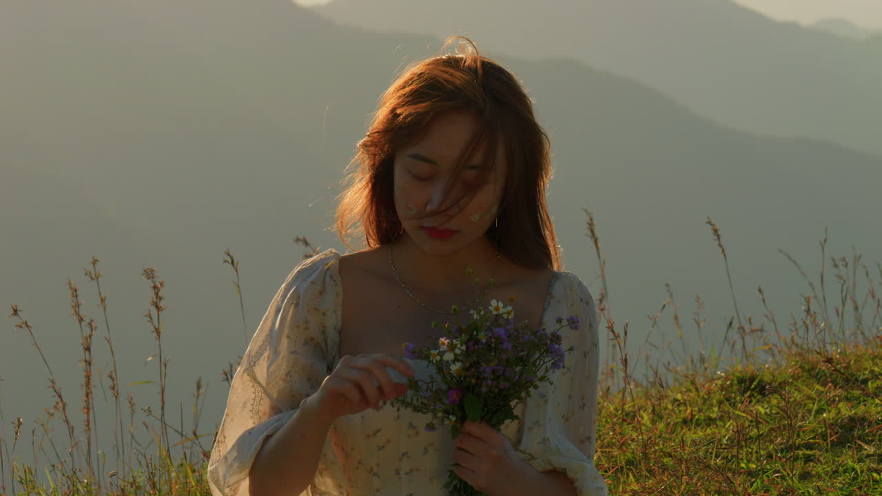 asiatic red hair female woman holding a bouquet of flower standing alone in nature forest at sunset wearing elegant white dress