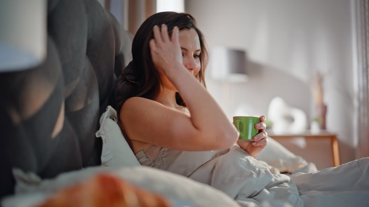 Woman holding coffee bed watching movie at laptop closeup. Smiling lady lying
