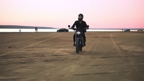 Front-view-of-young-biker-in-helmet-and-jacket,-man-is-riding-at-sport-motorbike.-Wind-blowing,-water-front