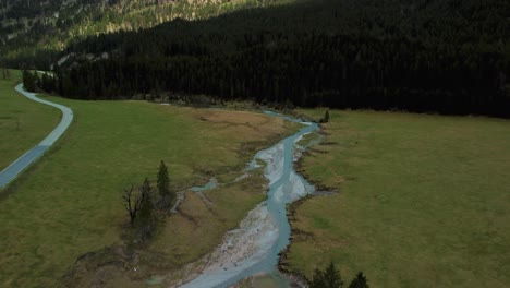 drone flight along a scenic mountain river with fresh blue water in the bavarian austrian alps on a cloudy day, flowing down a riverbed along trees, rocks, forest and hills seen from above by drone