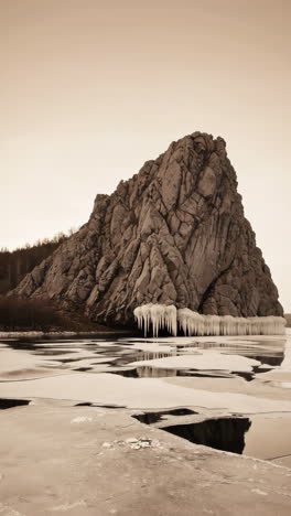 dramatic rocky cliff with icicles over frozen water