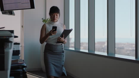 asian-business-woman-using-smartphone-walking-through-office-texting-sending-messages-successful-female-executive-checking-emails-on-mobile-phone-in-workplace