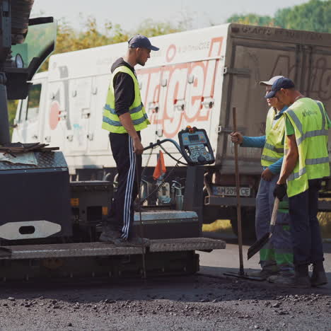 team of workers and asphalt machine outdoors in autumn. men workers in special clothing work on the road during asphalting.