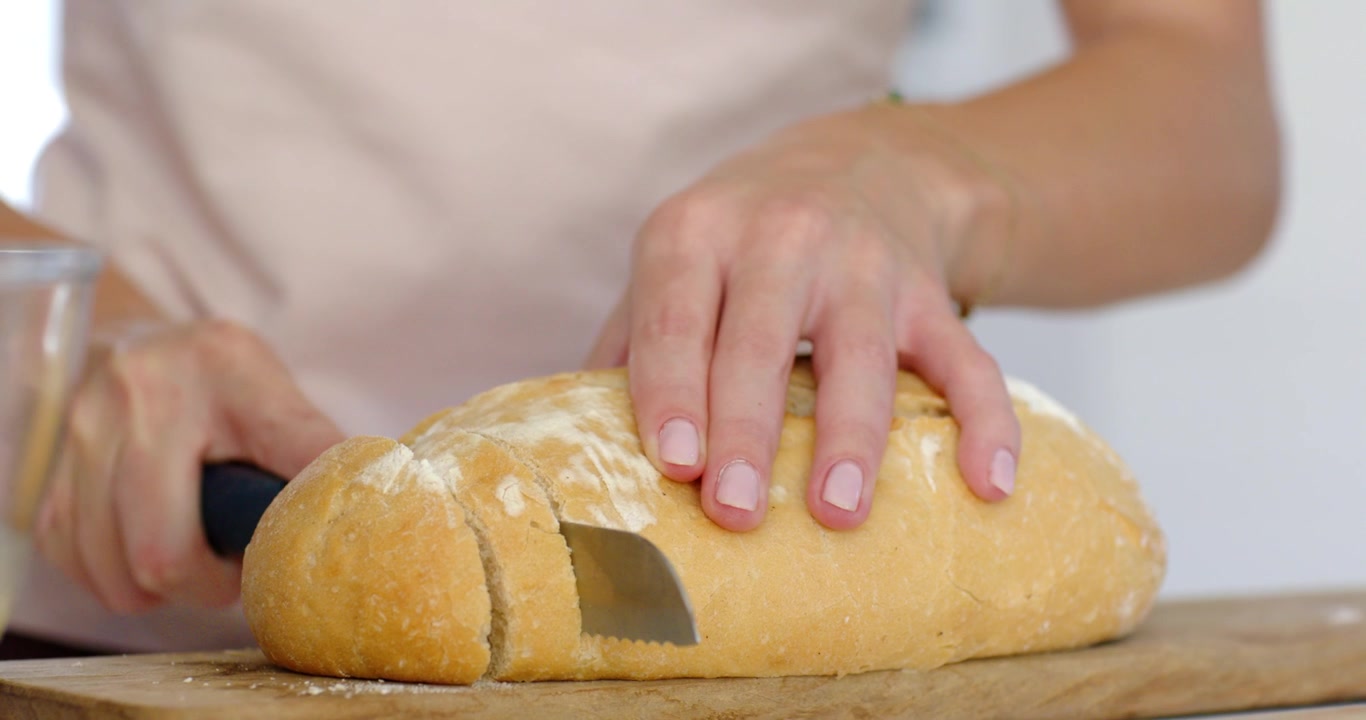 Mani di donna adulta che premono la lama nel pane, segando con un coltello seghettato per creare fette su un tagliere