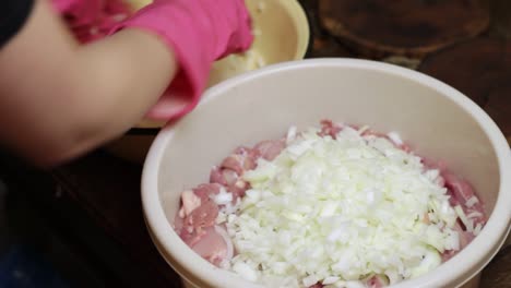 gloved hands adding chopped white onions into a bowl of raw chicken for shashlik