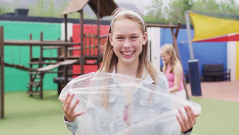 Portrait-of-happy-caucasian-schoolchildren-cleaning-with-bags-at-school-playground