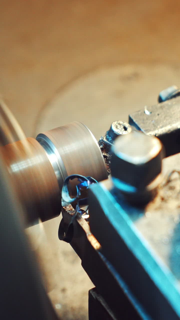 A cutter of lathe is sharpening metal billet for production at the plant. Thin shavings are falling on the surface of the equipment. Close-up. Vertical video
