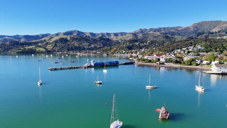 drone captures serene akaroa bay with boats, calm waters, and scenic hills under clear skies