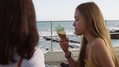 vista lateral de una chica caucásica comiendo helado en la playa con su amiga