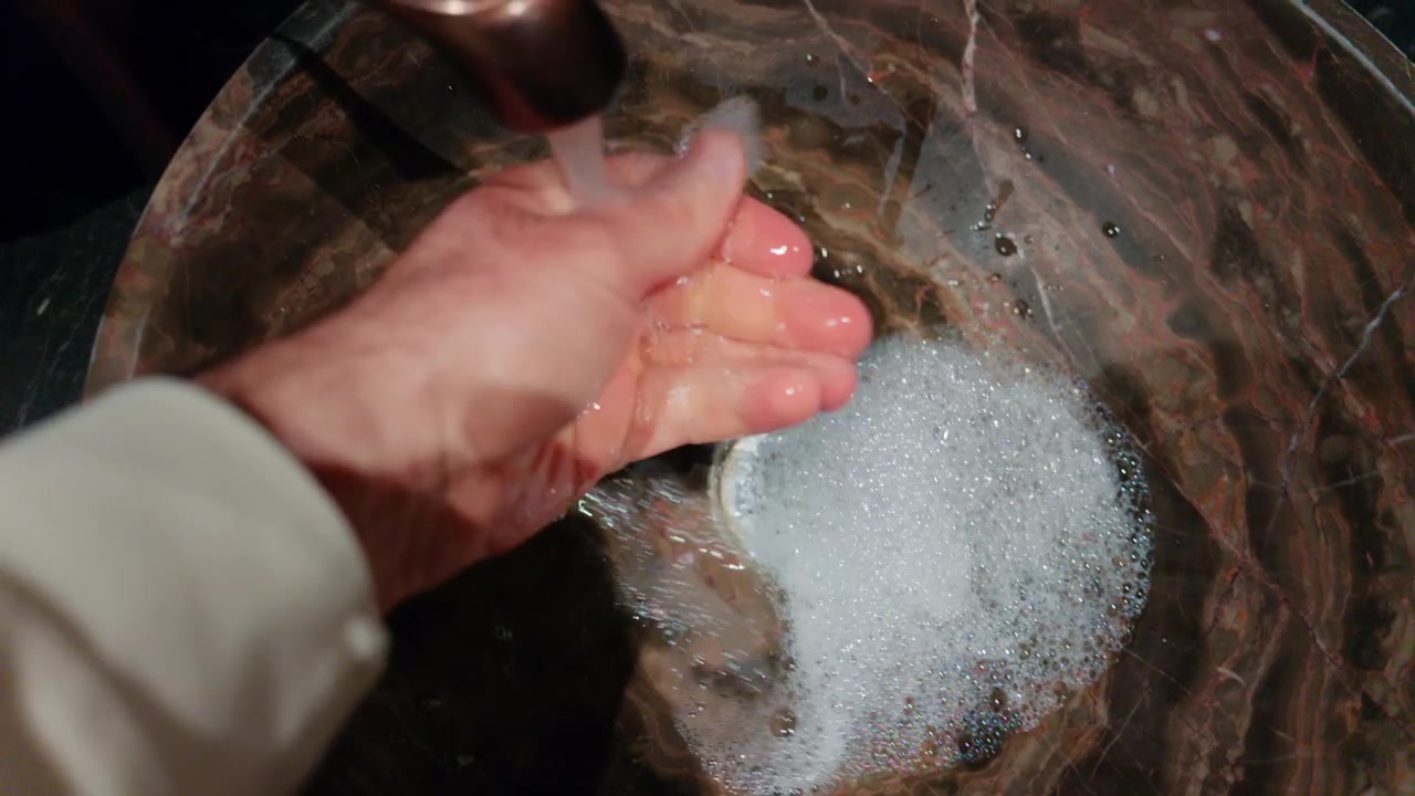 Persona lavándose las manos con jabón bajo el agua corriente en un lavabo.