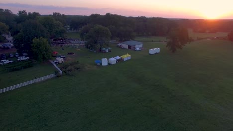 fly over 4k drone slow push in of rural music and art festival on historic farm at sunset