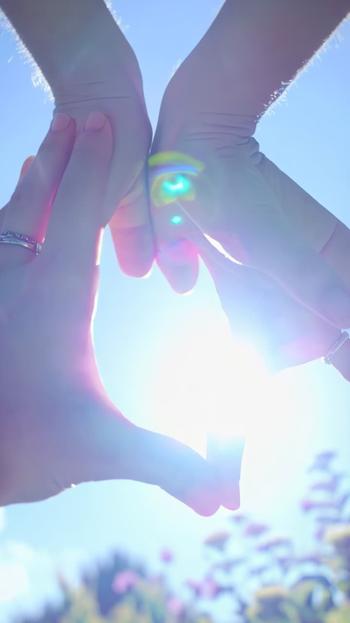 Hands forming a heart shape against the bright sunlit sky