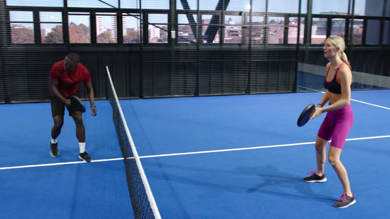 Man and woman playing padel tennis on blue indoor court, focused and enjoying game