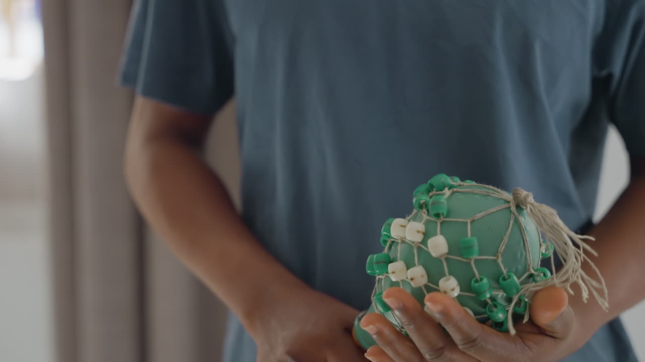 Closeup hands holding beaded scrubber, gentle indoor chore, seated person inspecting green beaded brush, slow careful motions, soft natural light, neutral curtains, intimate domestic routine