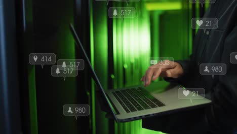 animación de iconos de redes sociales sobre la sección media de un ingeniero masculino usando una computadora portátil en la sala de servidores.