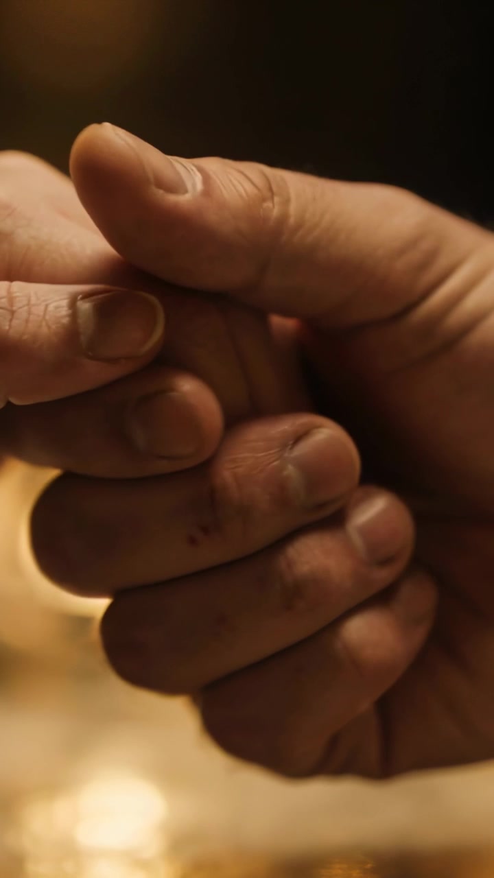 Vertical video: Touching larger hand holding smaller hand for help on glass table, with warm light