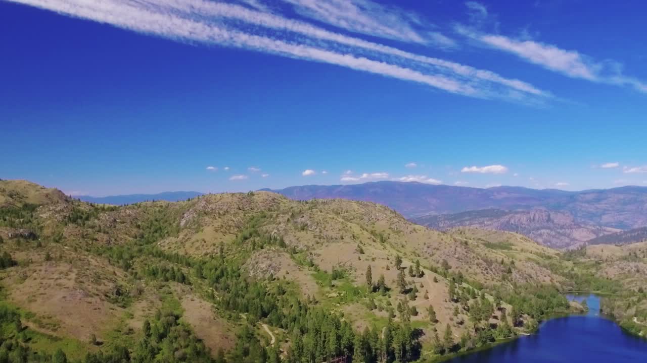 drone disparó panorámica justo entonces tirando lejos revelando un impresionante paisaje de árboles, montañas y un lago en un brillante día soleado