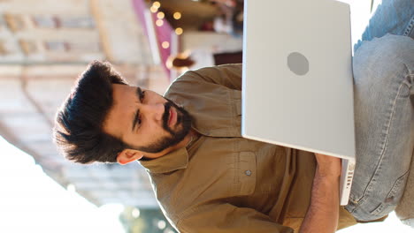 Indian-man-sitting-in-city-street,-use-laptop,-loses,-fortune-loss,-fail,-online-bad-news,-play-game