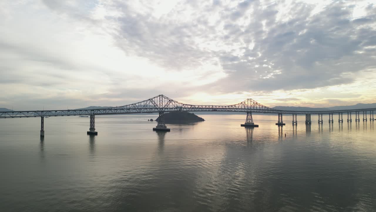 High-angle drone footage follows the Richmond–San Rafael Bridge at sunset as it spans the bay near Point Molate Beach.