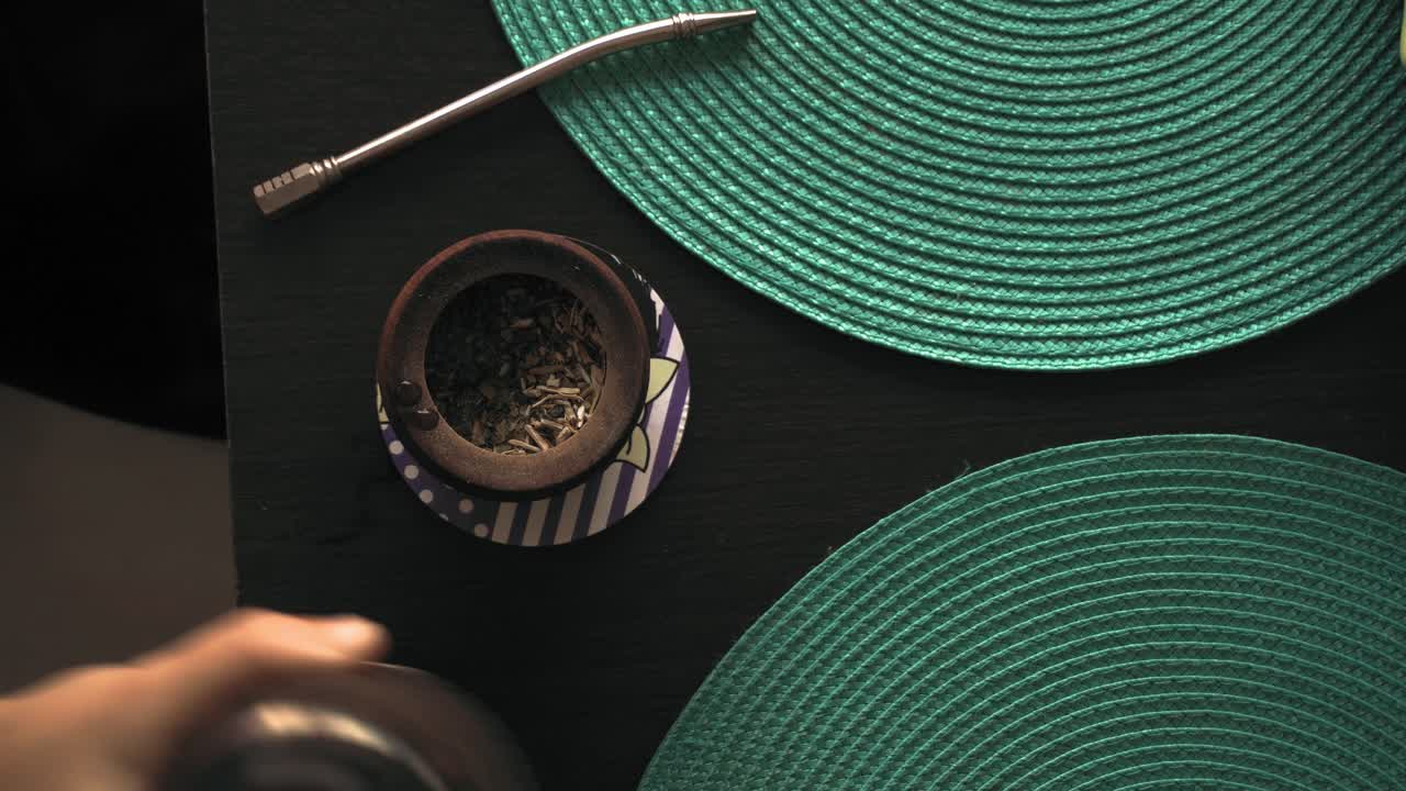 verter agua caliente en una taza, preparar té suelto de yerba mate.