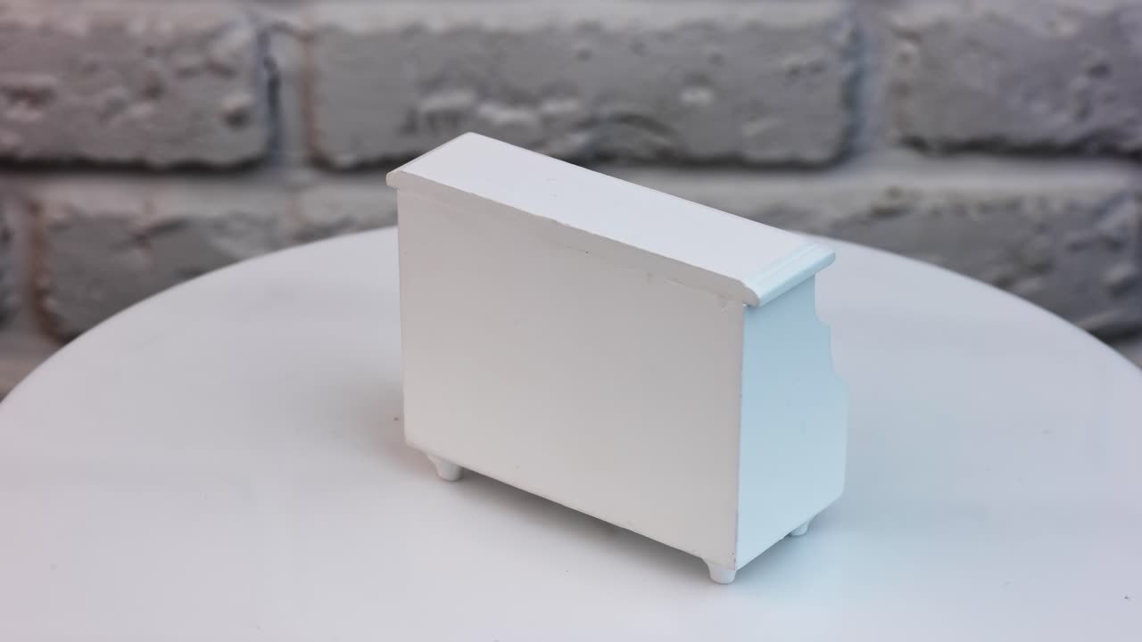 Little cupboard with two drawers and a shelf spinning around. Doll's house furniture against the white wall backdrop.