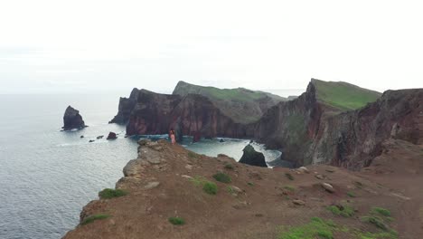 Una-Mujer-Está-Sola-Con-Un-Vestido-Rojo-Rosa-En-El-Viento-Al-Borde-De-Un-Acantilado-En-Madeira