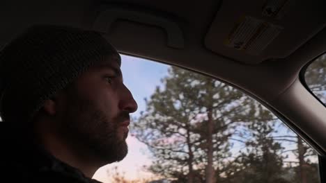 interior care shot of a young millennial male in a beanie driving through a sunset mountain landscape