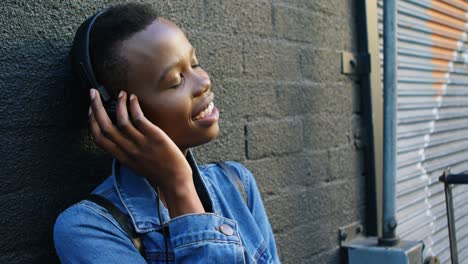 Woman-listening-music-on-headphones-while-leaning-against-wall-4k