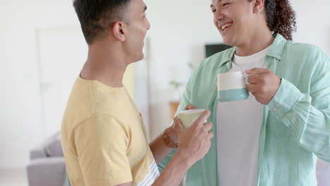 happy diverse gay male couple having coffee, standing and talking at home, copy space, slow motion