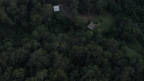 flying over a thickly wooded forest looking down on a small property tucked in the jungle