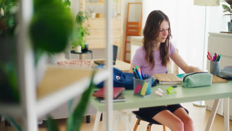 a young student sits at her desk and looks through her math notebook and starts studying for school