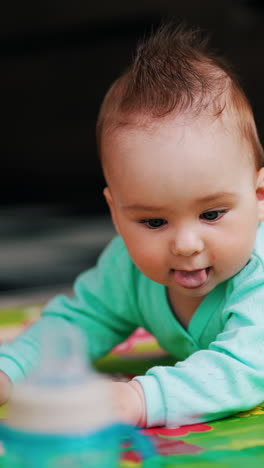 nice little caucasian toddler lies on the mat. baby pays attention to a bottle standing beside. blurred backdrop. vertical video