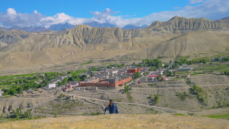 Male-Tourist-enjoys-scenic-beauty-during-trekking-uphill,-Lomanthang-village-of-Upper-Mustang-Nepal-and-dry-strange-hills-in-backdrop-with-huge-inhabitation-of-people