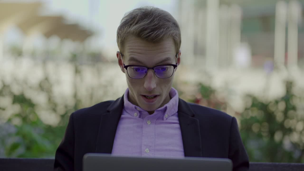 восторженный молодой человек сидит в парке с ноутбуком