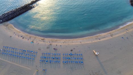 Aerial-view-of-Los-Cristianos-beach-with-clear-blue-water,-sun-glare-in-ocean,-Canary-island,-Spain