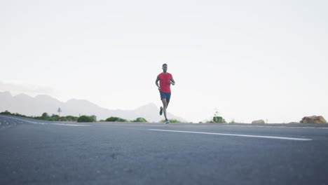 hombre afroamericano vestido con ropa deportiva corriendo por la carretera