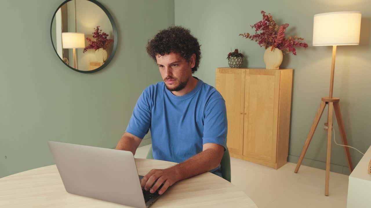 Uomo con i capelli ricci che digita sul laptop alla scrivania dell'ufficio di casa