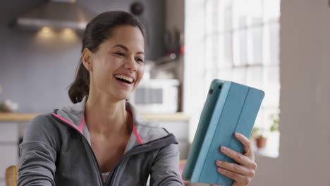 Feliz-Mujer-De-Raza-Mixta-Hablando-Con-Su-Amiga-En-Línea-Usando-Una-Aplicación-De-Tableta-Digital-En-Casa-Usando-Ropa-Deportiva