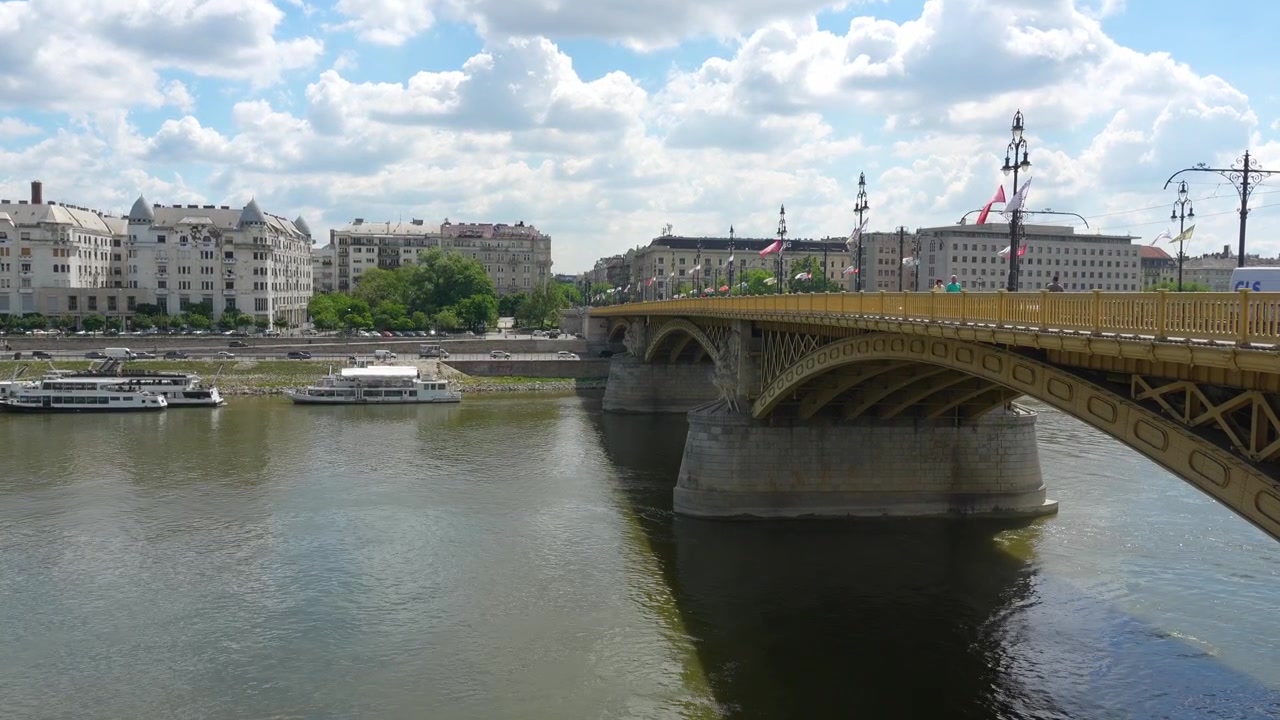 Ponte Margherita che attraversa il Danubio a Budapest, Ungheria. Luminosa luce diurna estiva, barche sull'acqua, architettura storica lungo il fiume, ampio panorama urbano