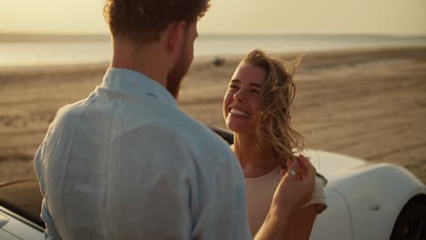 une fille heureuse étreint son petit ami dans une chemise bleue près d'une voiture blanche. une réunion d'été romantique contre la rivière et le ciel jaune