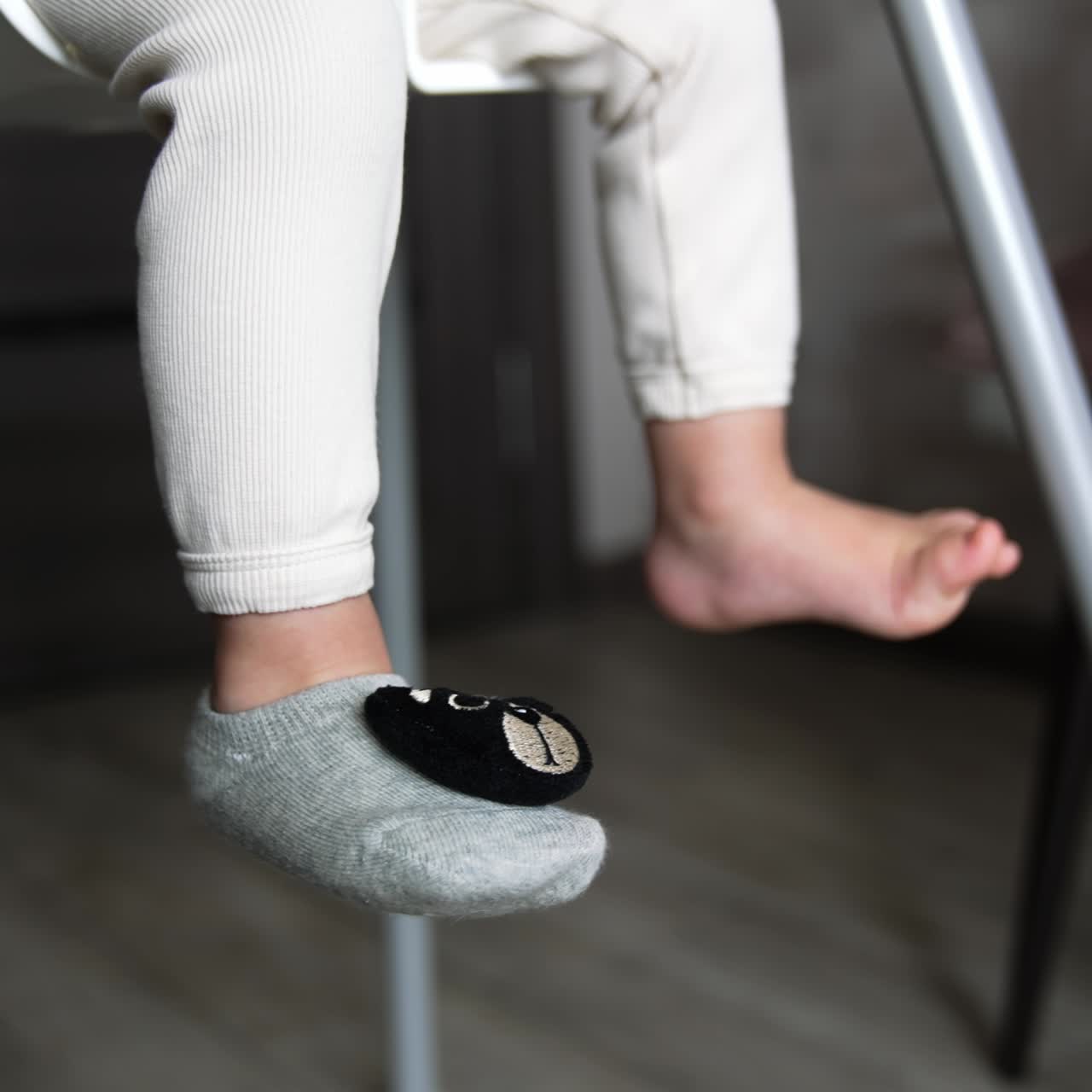 Adorable feet of a little baby sitting on the chair. One foot is bare and the other is in sock with teddy bear face on. Close up