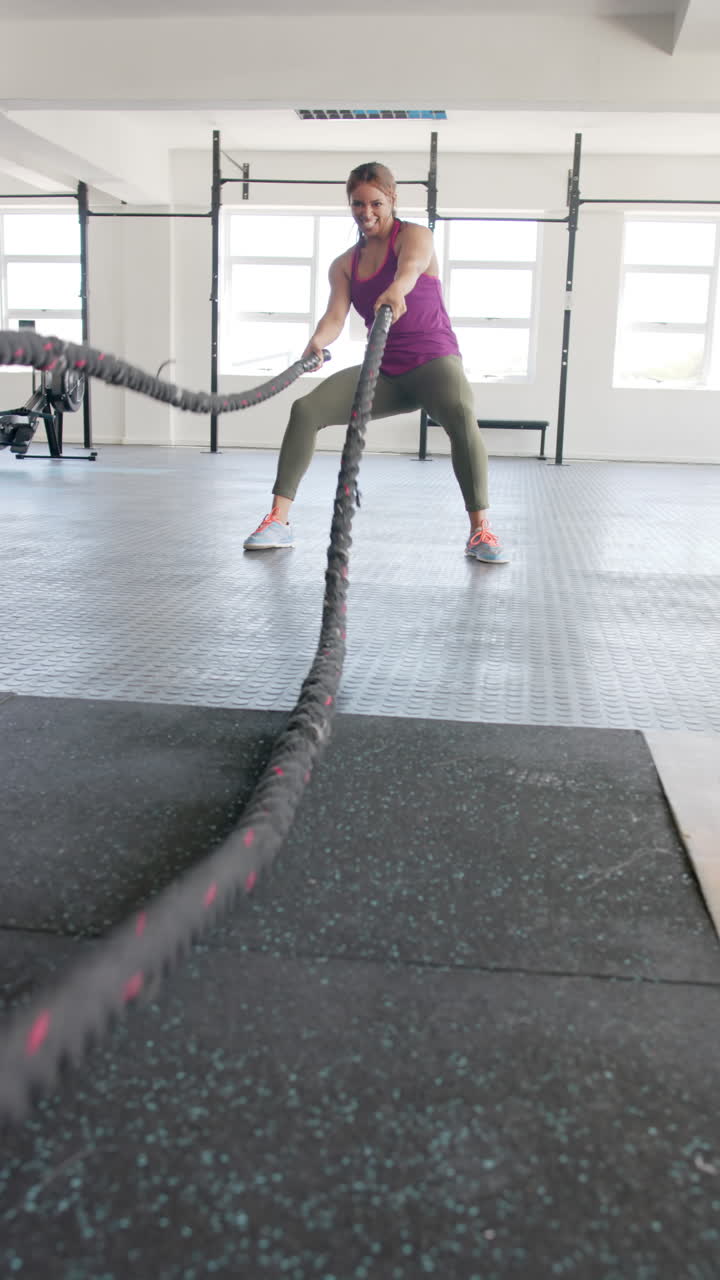 Vertical video of focused biracial sports woman exercising with lines at gym in slow motion
